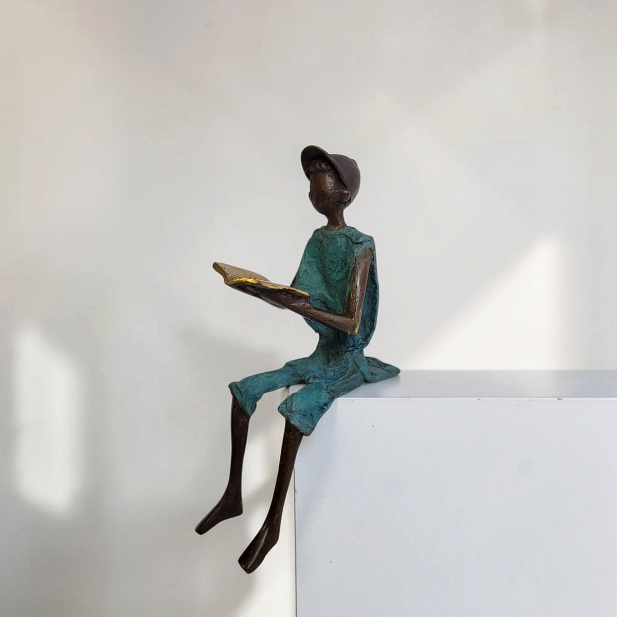 Bronze-Skulptur "Hugo" Enfant avec livre et casquette | by Souleymane