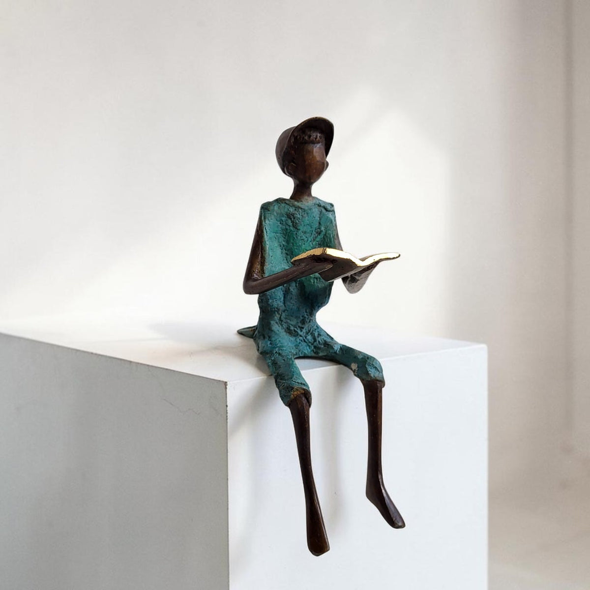 Bronze-Skulptur "Hugo" Enfant avec livre et casquette | by Souleymane